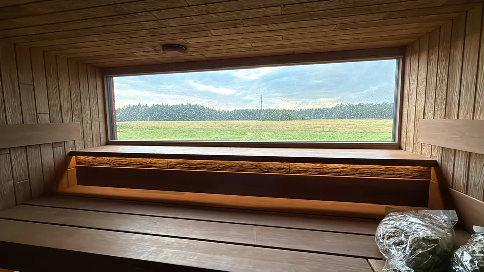 Panorāmas logs virs koka lāvas ar skatu uz ūdeni un pļavu